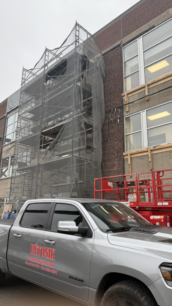 Bétonik truck parked near scaffolding at a concrete repair site, showcasing professional equipment and the ongoing restoration work on a building in Montreal.