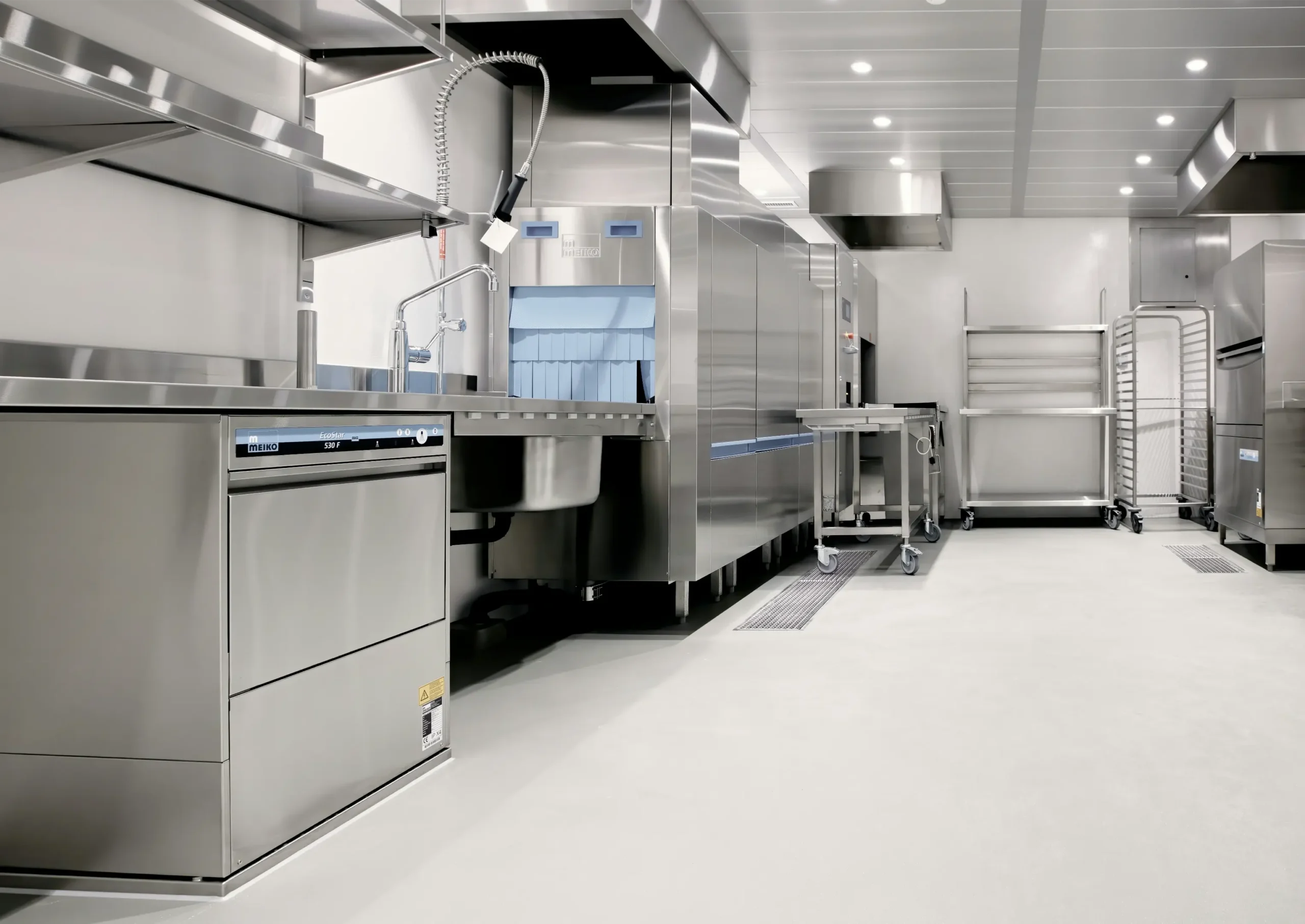 Cuisine commerciale moderne avec revêtement de sol en époxy, équipements en acier inoxydable, et espace de travail bien éclairé.