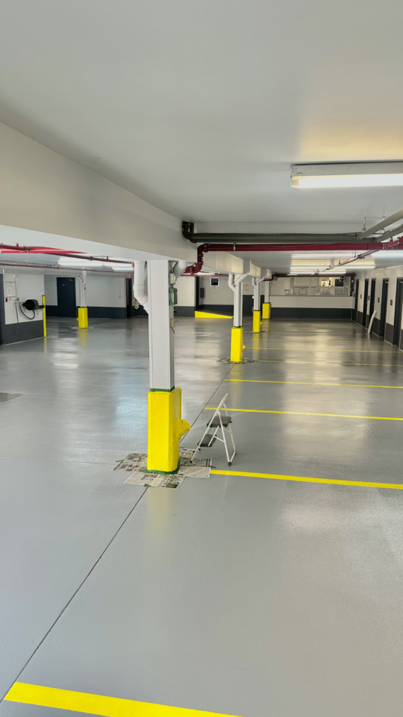 Interior commercial parking garage with freshly painted concrete floor, yellow-striped parking spaces, and yellow-painted support columns.