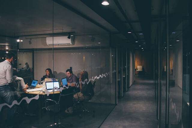 Groupe de personnes en réunion dans un bureau moderne avec ordinateurs portables, représentant l'équipe de Bétonik inc. discutant de projets de rénovation de sols en époxy.