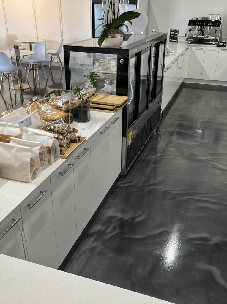 Seamless epoxy flooring in a commercial kitchen, featuring a glossy finish, resistant to grease and industrial cleaners, with a display of baked goods and a refrigerated unit in the foreground.
