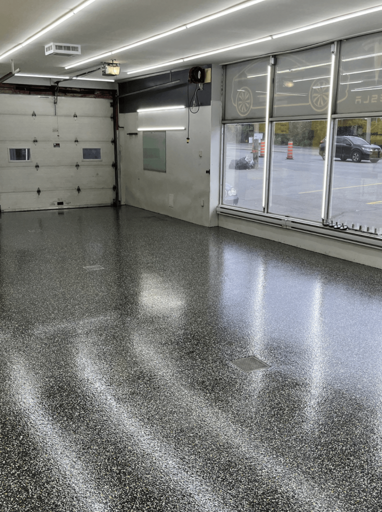Epoxy garage floor with a glossy finish, showcasing slip-resistant texture, in a well-lit garage setting with a garage door and large windows.