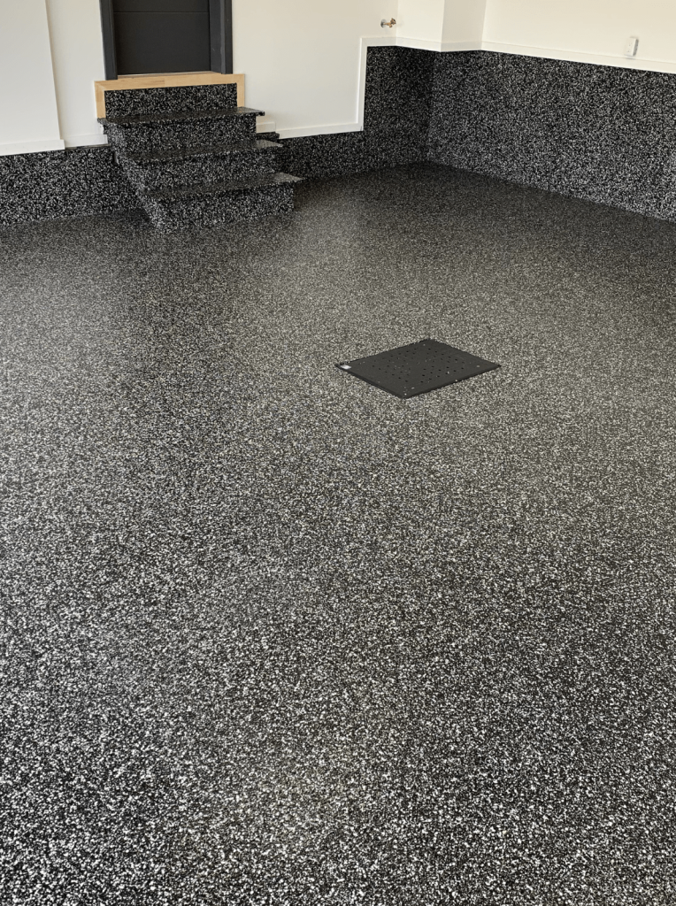 Epoxy garage floor featuring a modern granite look with integrated texture for grip, showcasing a blend of vinyl chips in a 100% solid finish, designed for durability and easy maintenance.