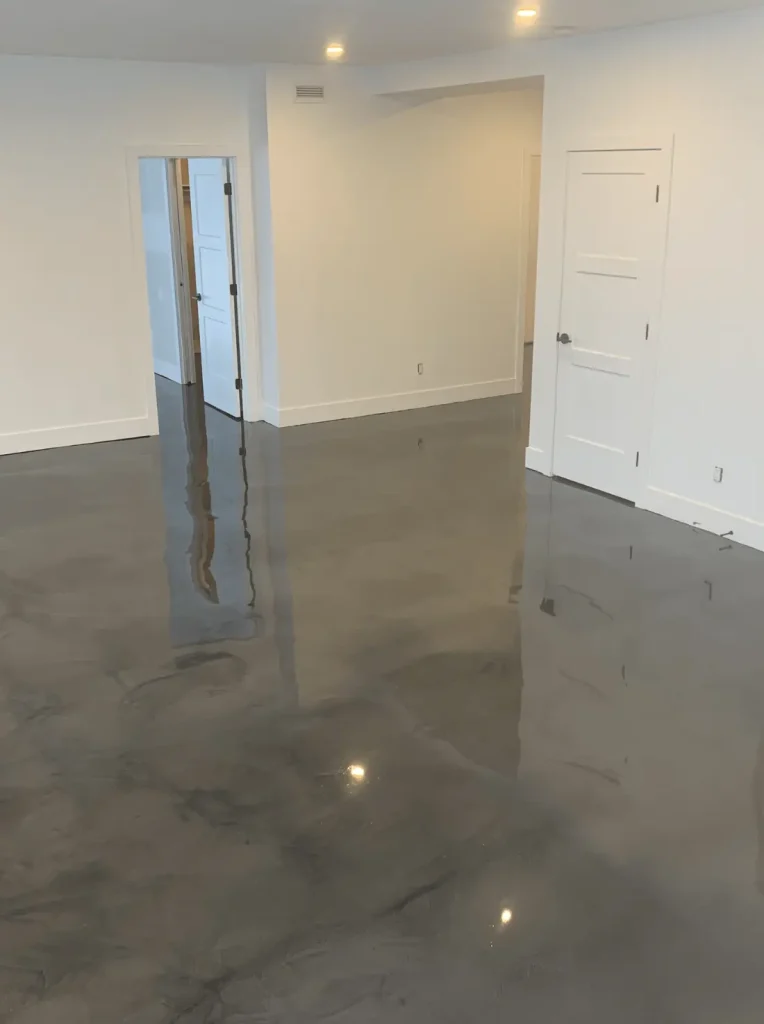 Modern epoxy flooring in a bright, spacious basement with reflective surface and white walls, showcasing a clean and elegant living space ideal for residential use.