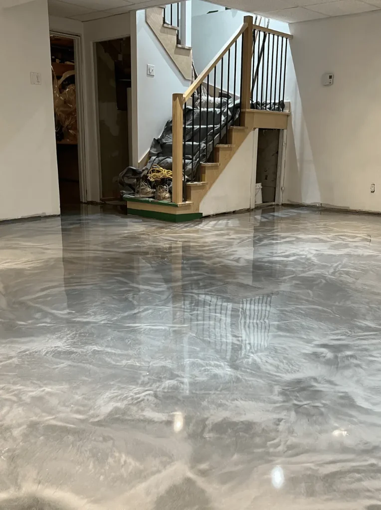 Basement interior featuring a polished epoxy floor with a marble-like finish, stairs in the background, showcasing high-performance flooring ideal for moisture protection and aesthetic appeal.