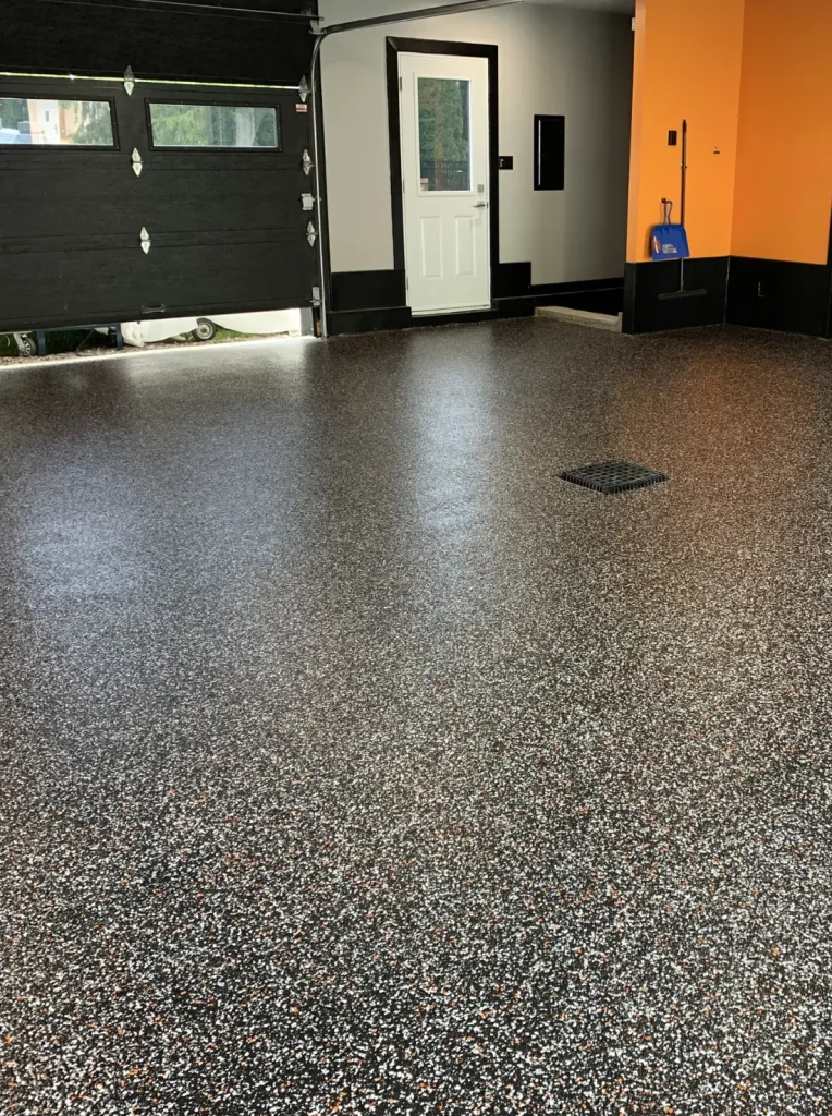 Plancher en époxy noir et gris brillant dans un garage, mettant en valeur une finition durable et résistante, avec une porte d'entrée et un mur orange en arrière-plan.