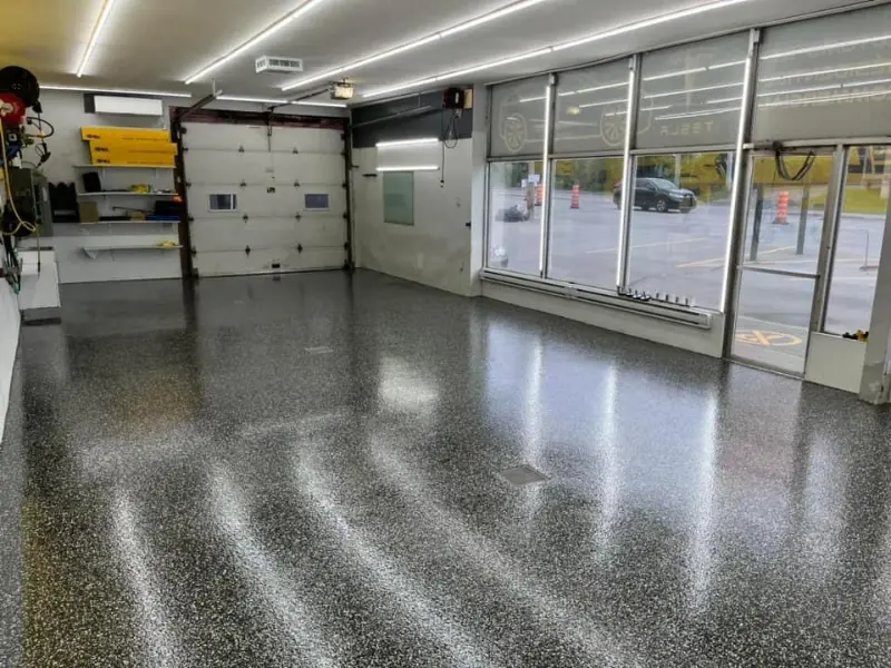 Garage with polished epoxy flooring featuring a custom flake blend, showcasing a clean and modern aesthetic, designed for high durability and easy maintenance, as part of a commercial detailing project by Bétonik Inc.