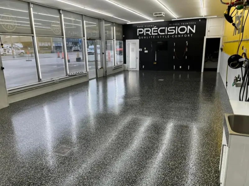 Intérieur d'un centre de detailing automobile avec un sol en époxy poli, logo "PRÉCISION" en arrière-plan, lumière naturelle à travers les fenêtres, espace propre et moderne, mettant en valeur l'esthétique showroom et la durabilité du revêtement de sol.