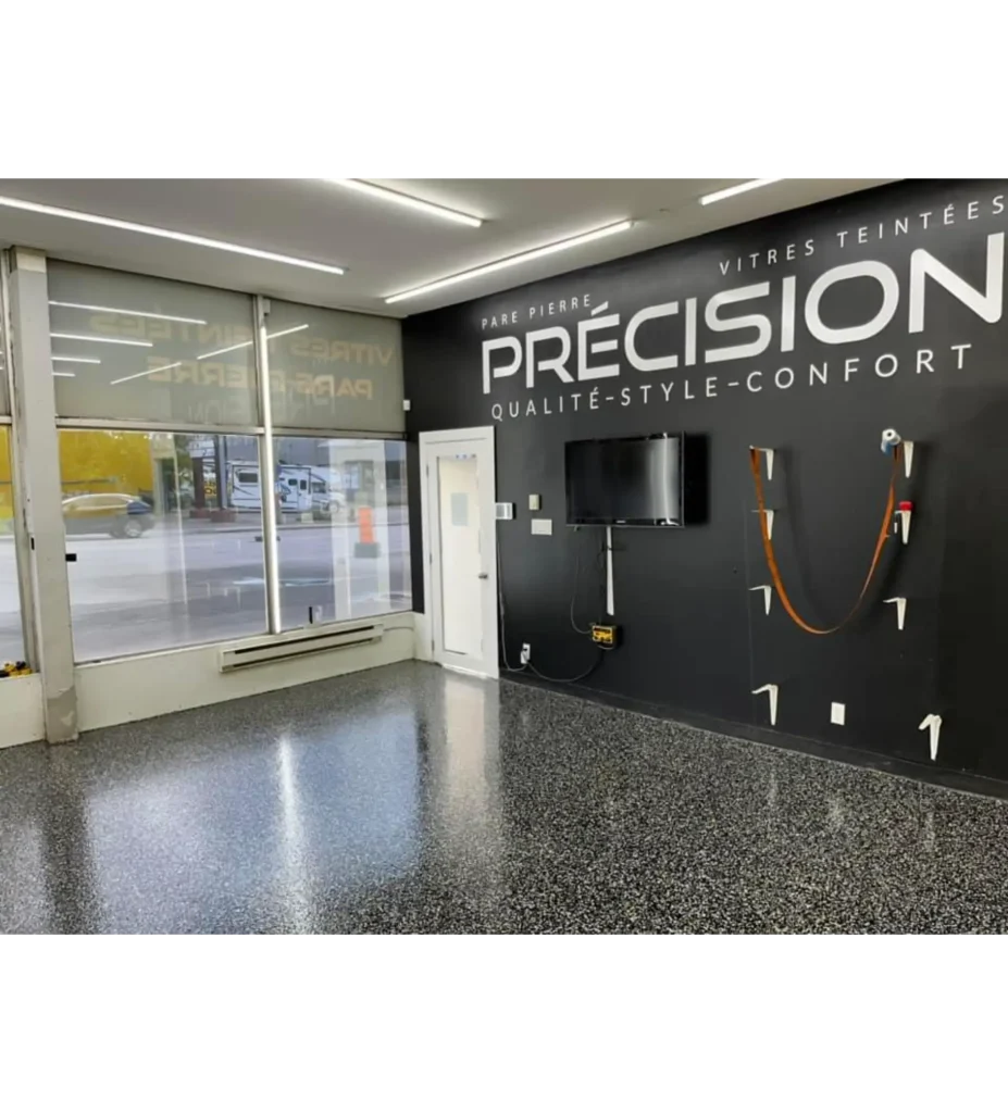 Intérieur d'un centre d'esthétique automobile avec un sol en époxy brillant, murs noirs avec le logo "PRÉCISION" et des équipements de finition de béton.