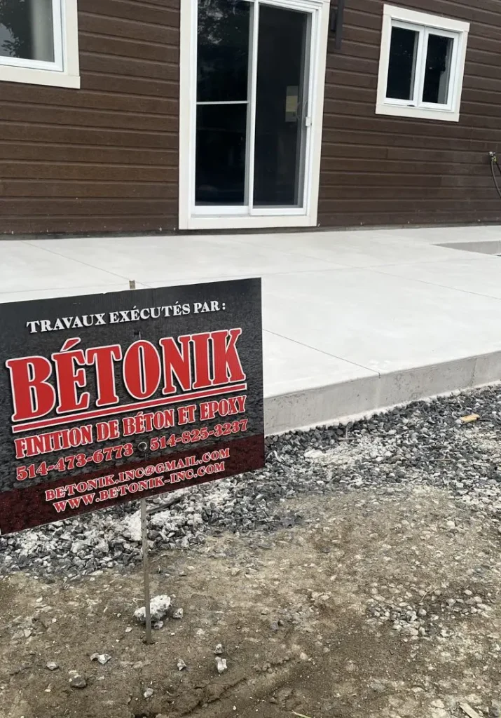 Panneau de signalisation de Bétonik devant une surface en béton fraîchement fini, mettant en avant les services de finition de béton et époxy de l'entreprise.