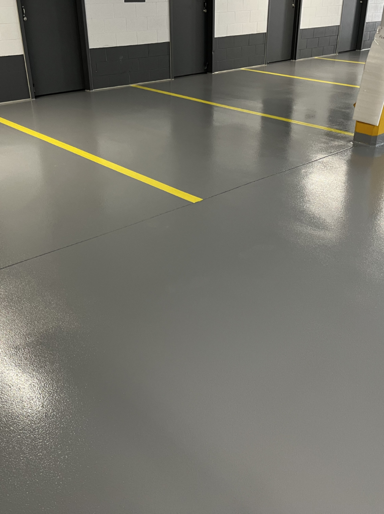 Revêtement de sol en époxy brillant dans un garage avec marquage au sol jaune, assurant durabilité et sécurité pour les véhicules et piétons.